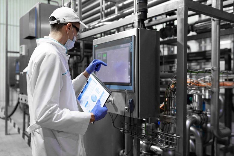 A scientist in a dairy shed, holding a clip board and using a touch screen.