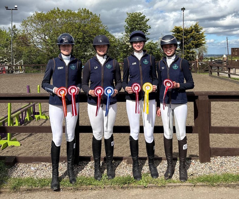 Four young women in equestrian gear, holding awards.