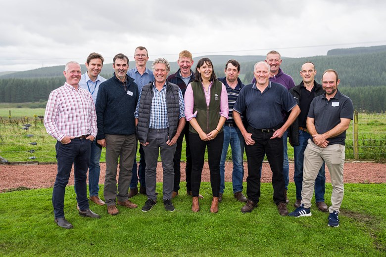 A group of men and one woman, posing for a photo on a farm.